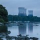 photo at dusk of river with rocks protruding and island in distance with 4 huge cooling towers with red lights