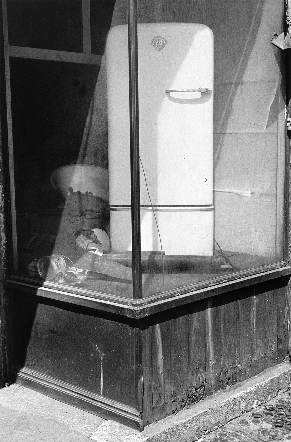black-and-white photo of abandoned retail window with white refrigerator displayed