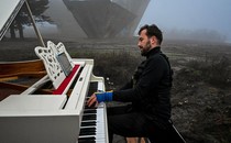 A person plays a piano outside on a foggy day, near a large concrete monument.