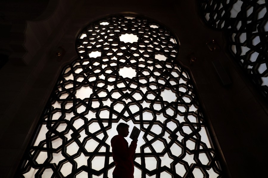 A person reads a book in front of an ornate mosque window.