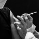 a vaccine being injected into an arm. both people in the photo are wearing masks. the tops of their faces are not visible.