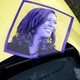 A purple poster of Kamala Harris rests on the hood of a yellow car