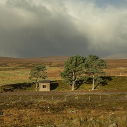 A small cottage stands below gray clouds with sun peeking through.