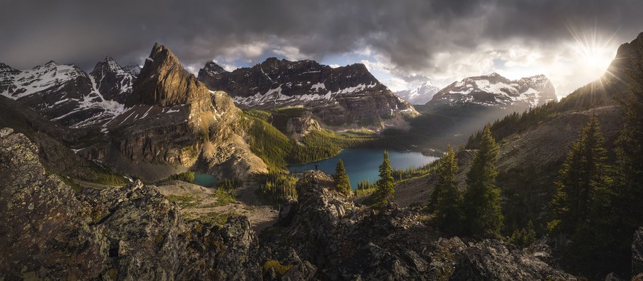 A panoramic view of a lake in a deep valley surrounded by dramatic rocky mountains.