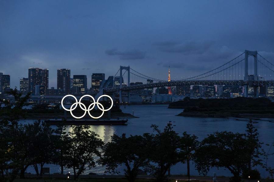 A night view of lit-up Olympic rings, with part of Tokyo's skyline in the background.