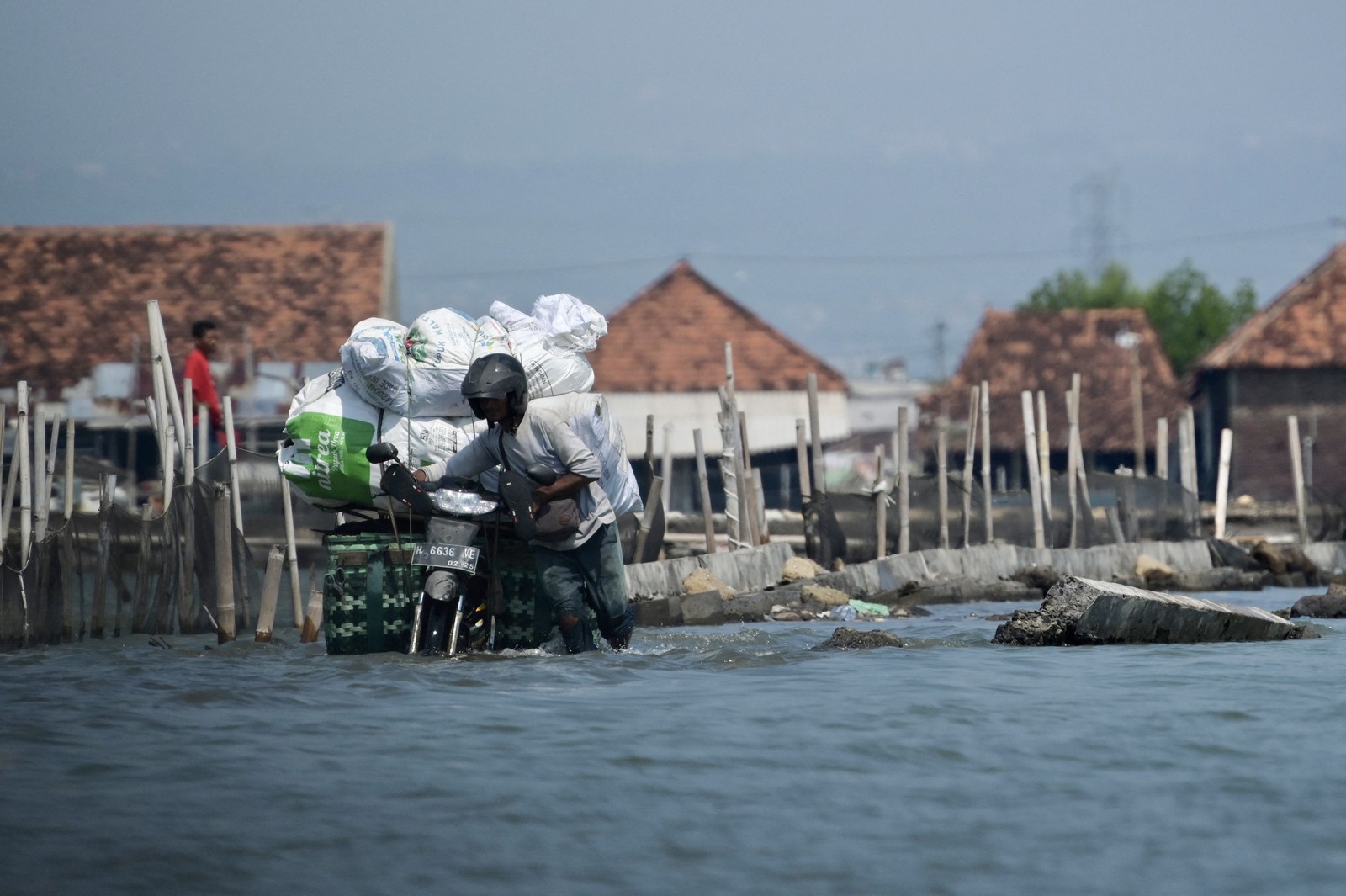 A person pushes a loaded motorcycle on a road submerged by seawater.