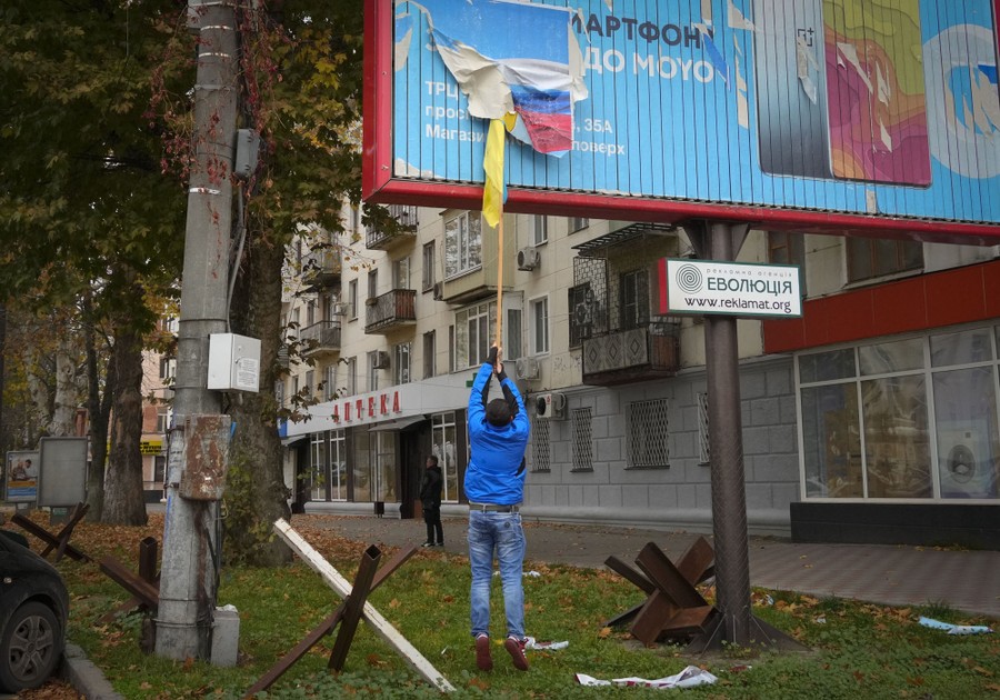 A local resident uses a long pole to remove the Russian flag from a billboard.