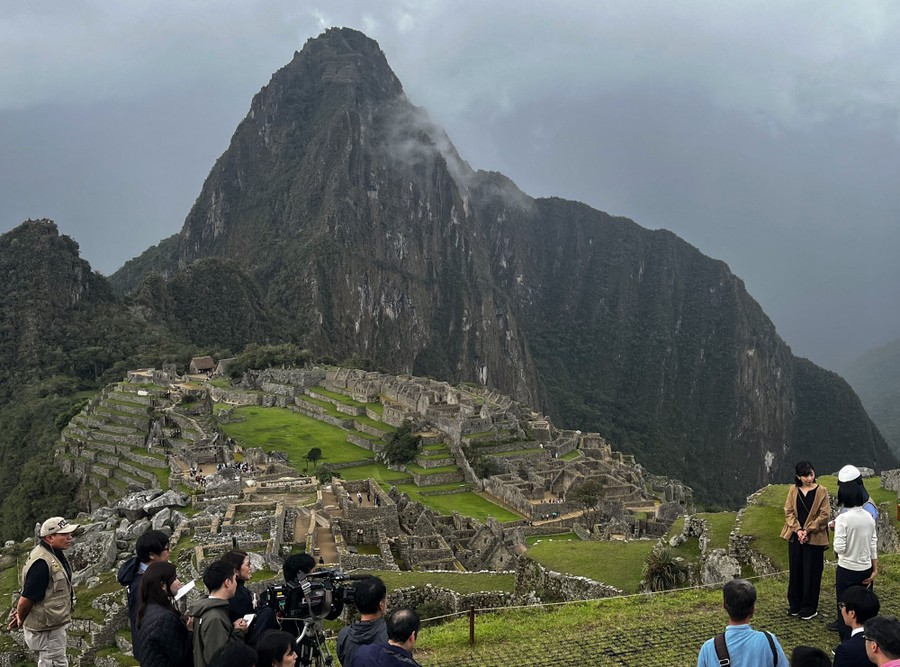 Photographers stand opposite a pair of people at an Incan citadel nestled in a mountain range.