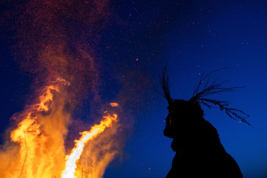 A person in costume watches a bonfire.