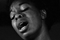 Nina Simone singing with her eyes closed, wearing a pearl necklace