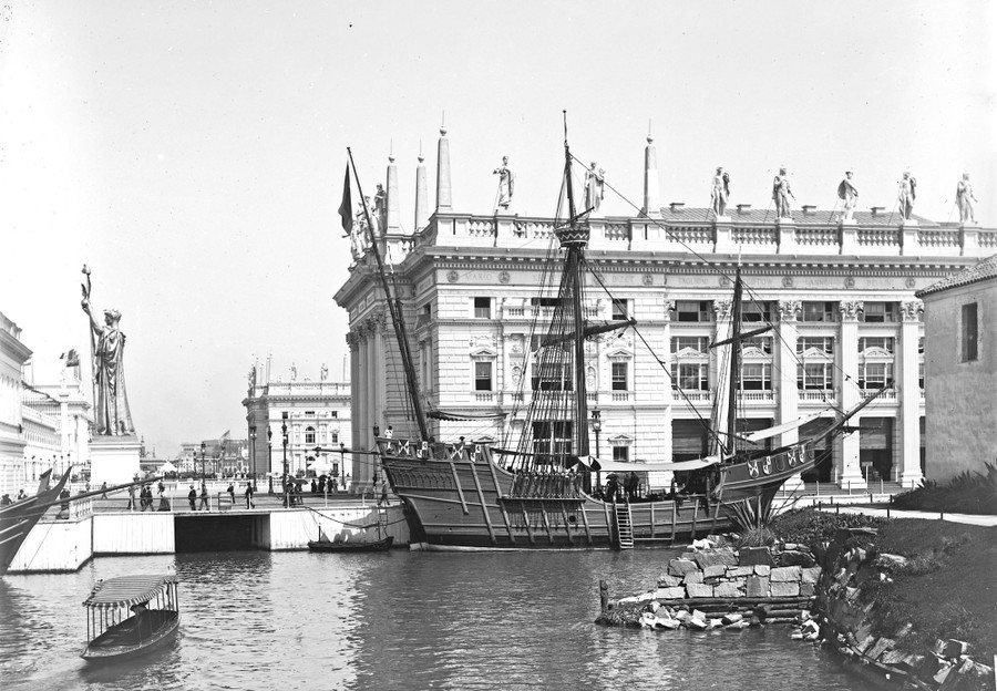 A replica of a historic sailing ship docked beside a large building