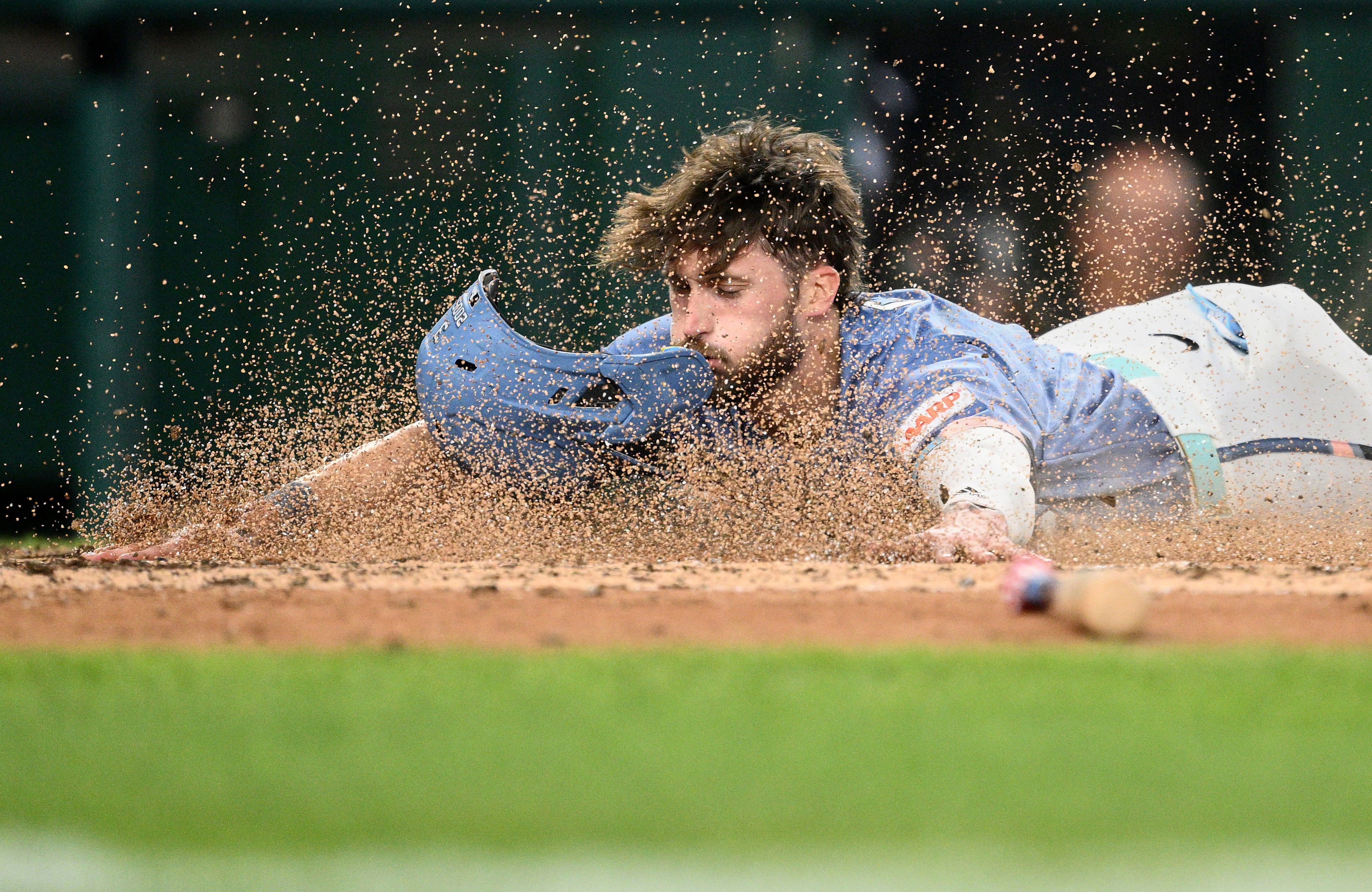 A baseball player slides headfirst into home plate, sending up a spray of dirt.