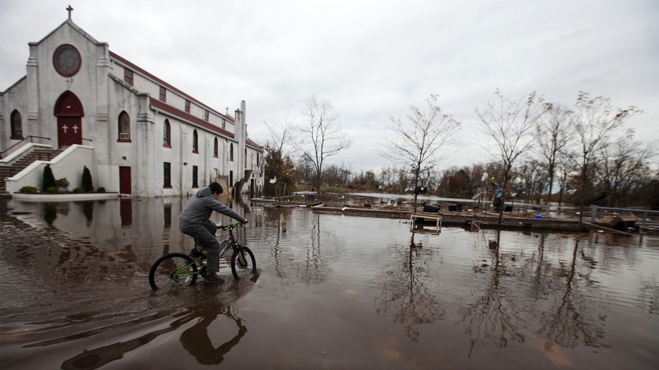 A person rides a bicycle past a church on a flooded street.