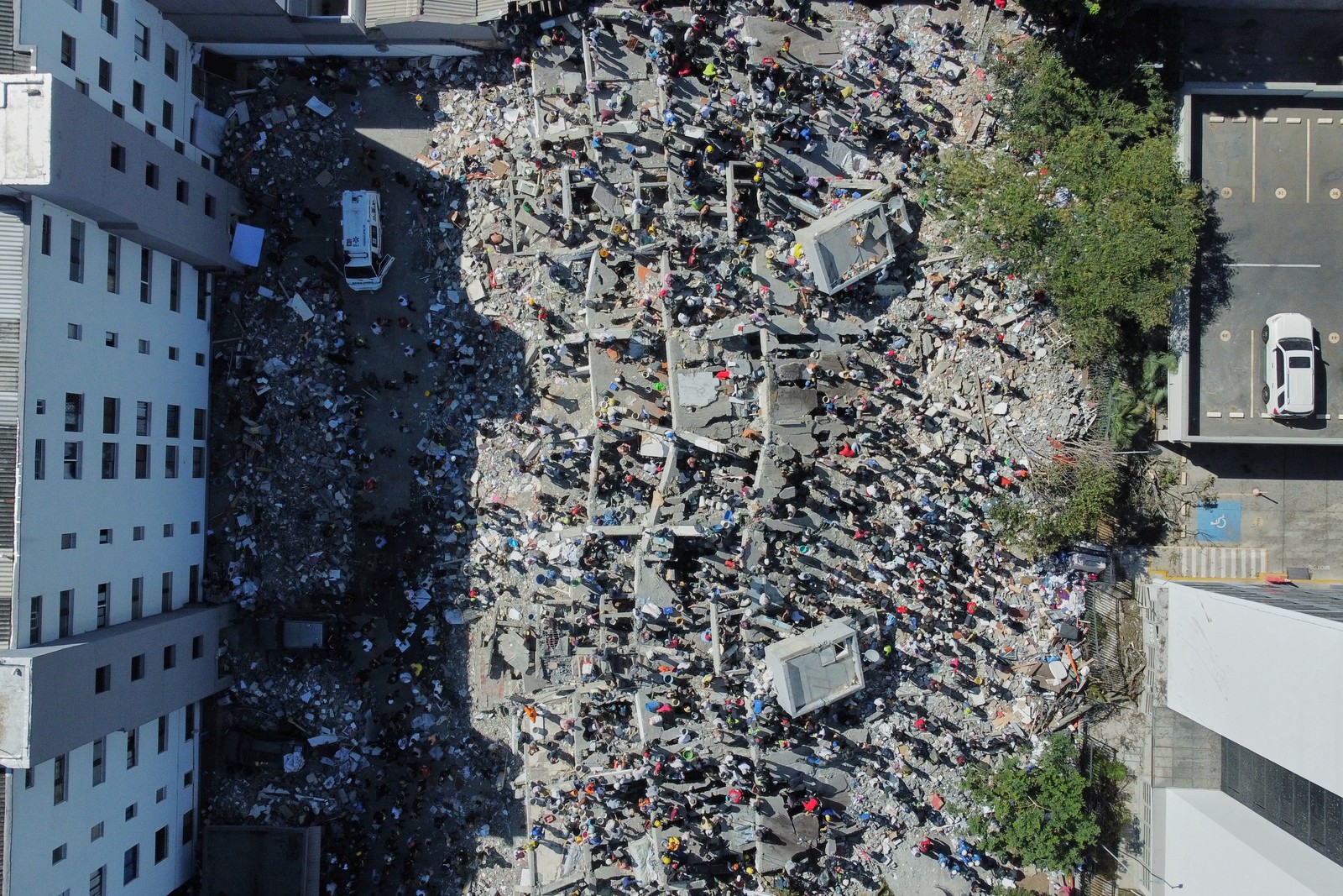A top-down aerial view of residents and rescue workers searching through rubble after an earthquake
