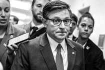 A black-and-white photo of Mike Johnson walking down a hallway, surrounded by other people