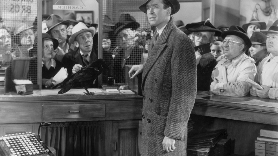 James Stewart stands behind a cashier's desk with a crowd of people in the background. (Hulton Archive / Getty)