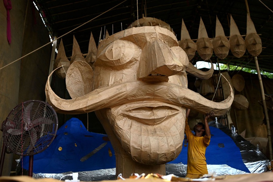 A person works on a large paper head of a demon with a handlebar mustache.