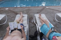 Two people sit in lounge chairs by a pool