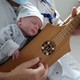 A newborn child rests on the chest of a person playing a traditional stringed instrument.
