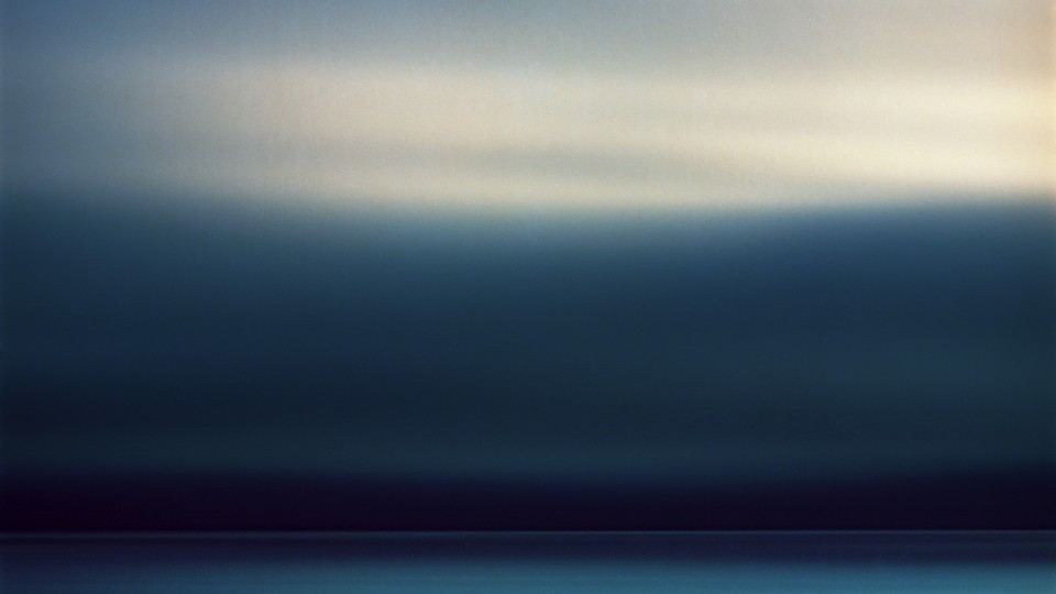 A long exposure of a passing storm over the horizon of the Pacific Ocean off the Oregon coast.  The long exposure renders the clouds as an abstract blur of motion and color and the setting sun highlights the higher clouds with a warm glow while the lower clouds are dark and brooding.