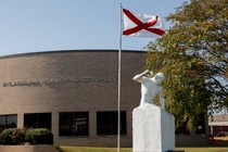 A brown building behind a sculpture and a flag pole of the Alabama flag