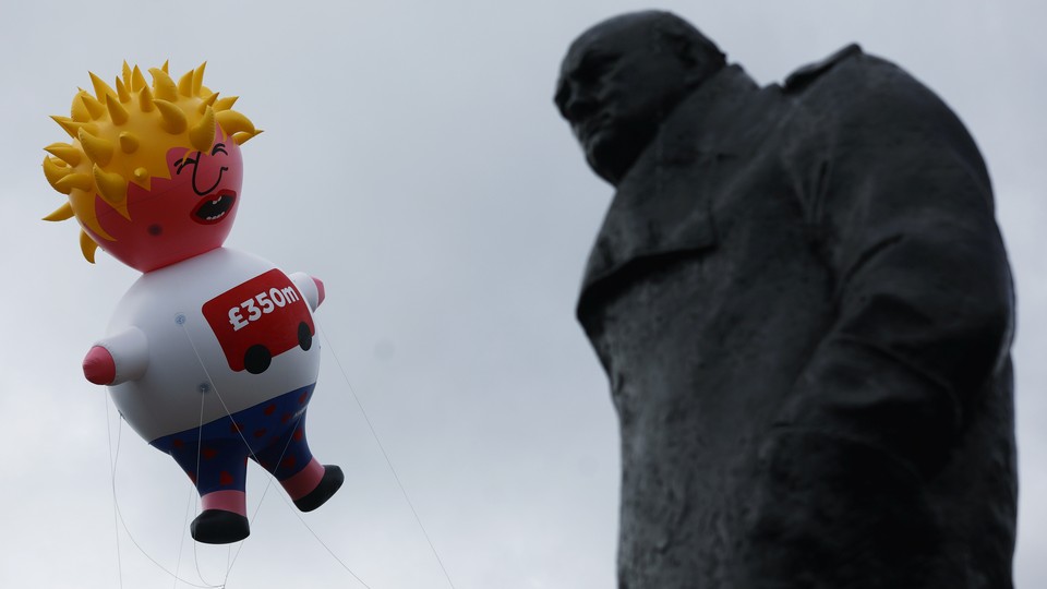 A giant inflatable blimp caricaturing Boris Johnson hovers beside a statue of Winston Churchill.