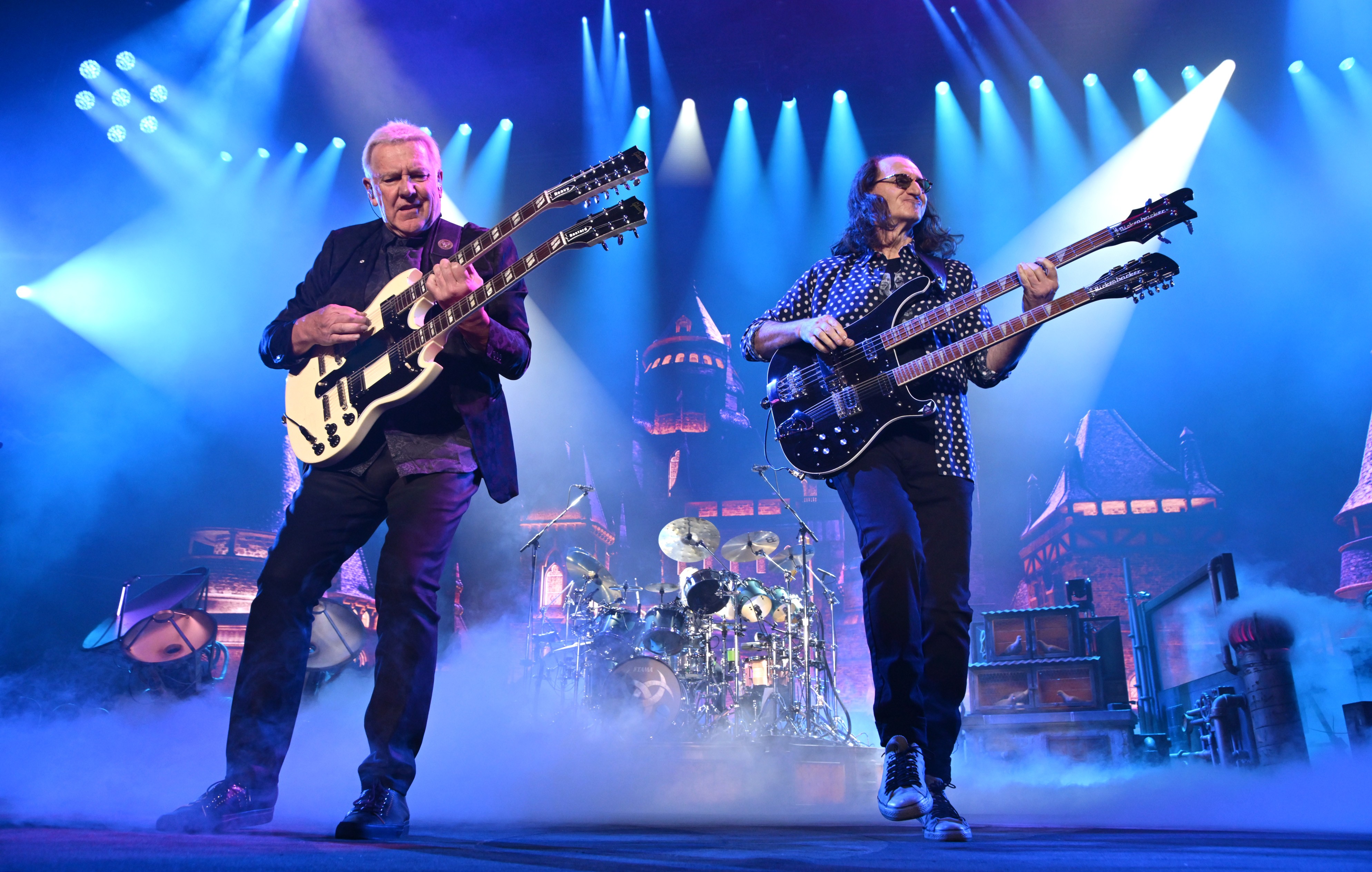 Alex Lifeson and Geddy Lee of Rush play guitars, performing on stage.