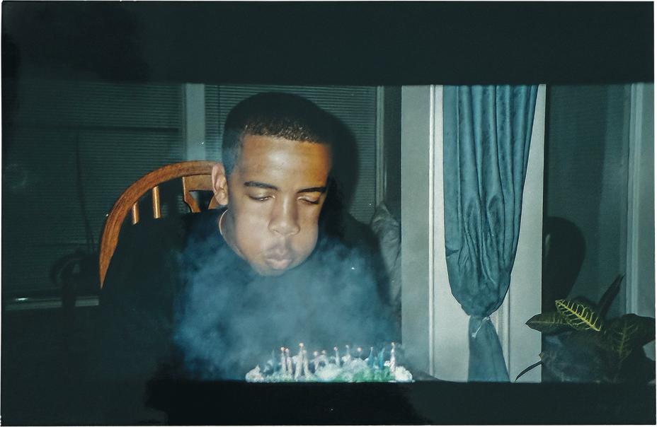 photo of young man with cheeks puffed out blowing out candles on cake