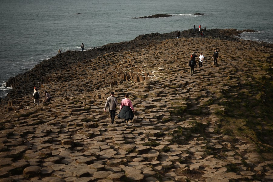 Visitors walk across an expanse of hexagonal basalt columns on a coastline.