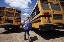 A girl walks toward two school buses. 