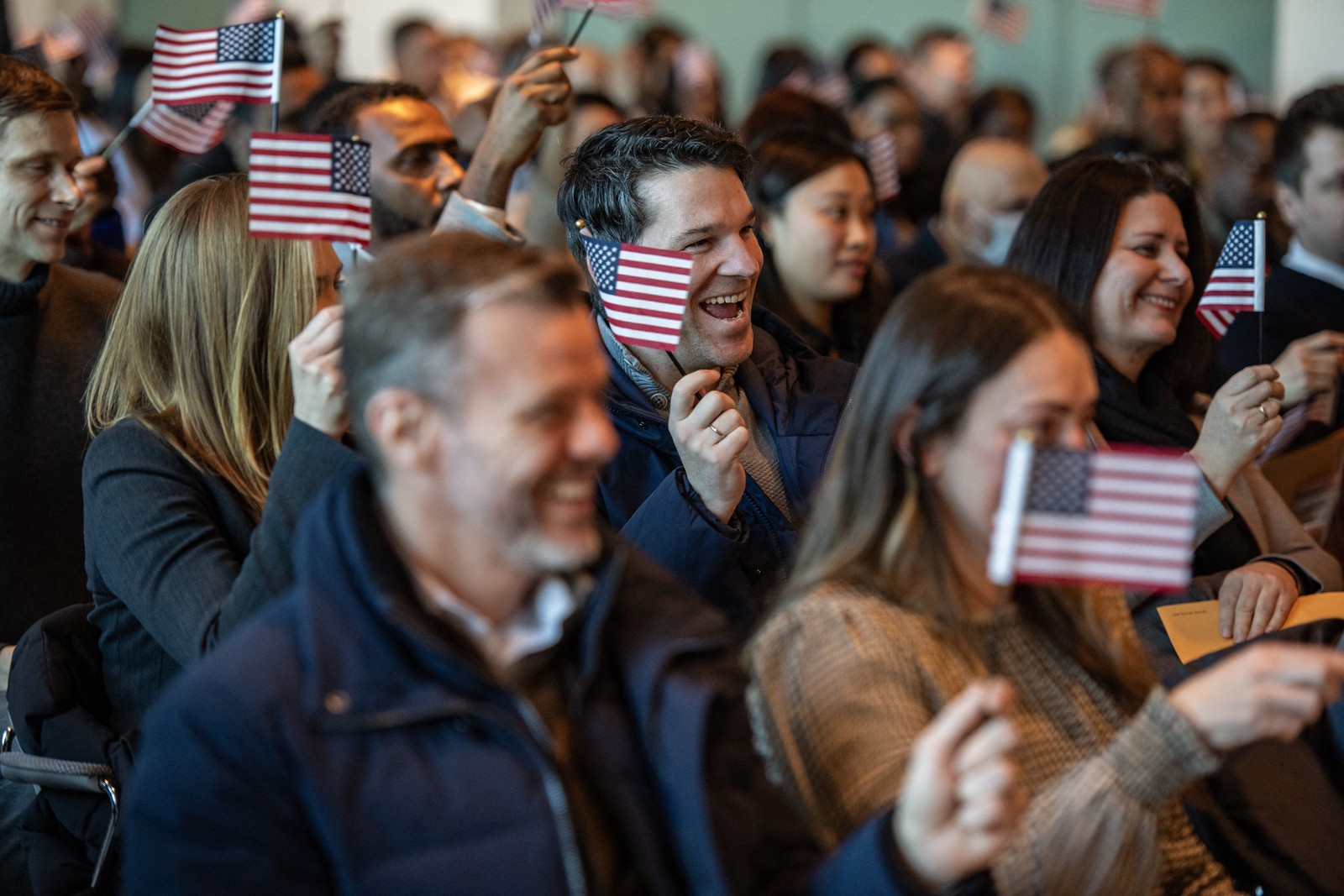 A small crowd of people, seated, wave American flags to celebrate becoming U.S. citizens after taking the oath of allegiance.