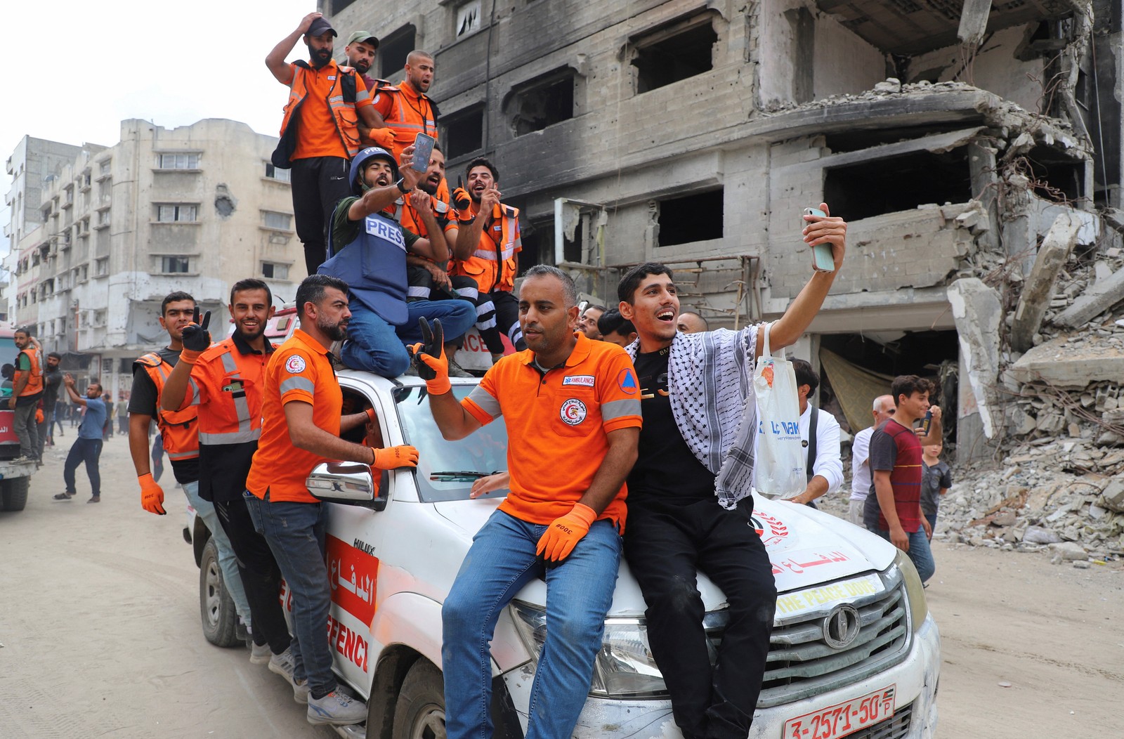 A group of emergency workers, most wearing bright orange vests, celebrate while riding in and on a small truck in Gaza.