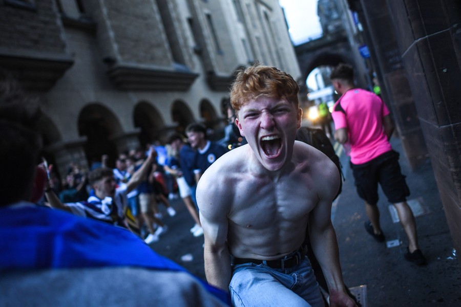 A shirtless Scotland fan celebrates with others in a street.