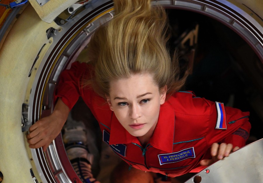 A woman moves through a hatch in the interior of a space station.