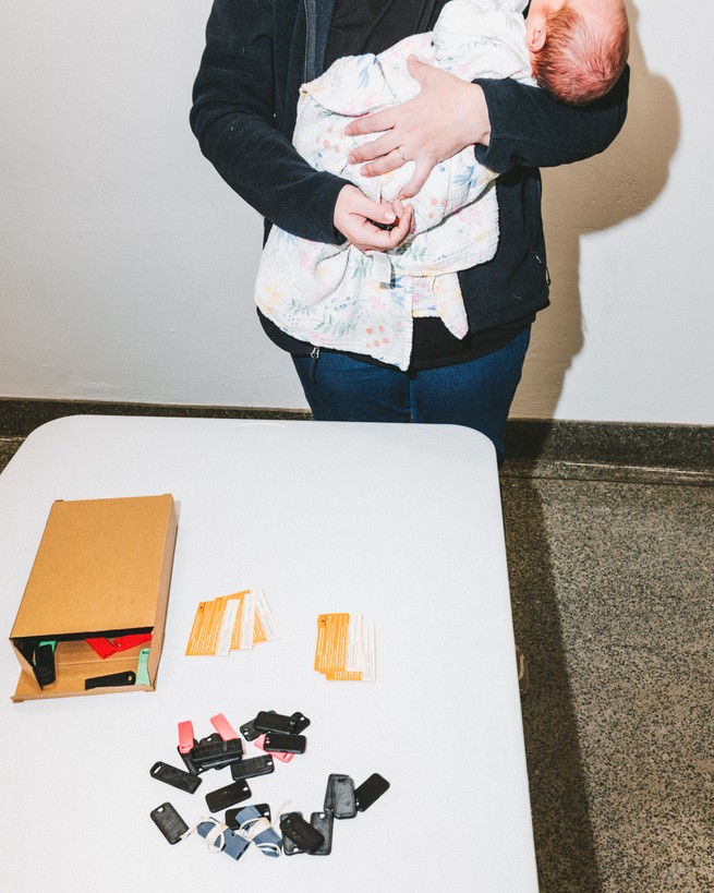 A woman holding a baby stands in front of a table with ICE whistles on it