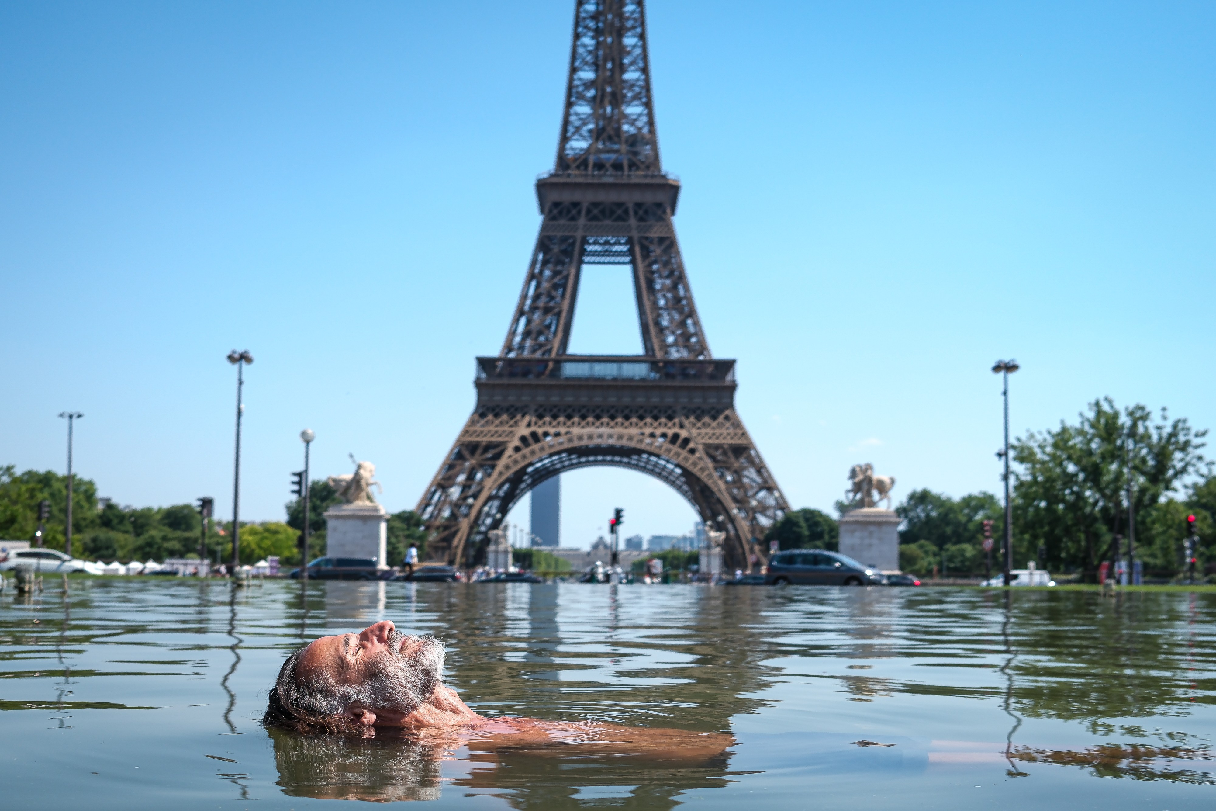 A man cools off, floating in a fountain in front of the Eiffel Tower.