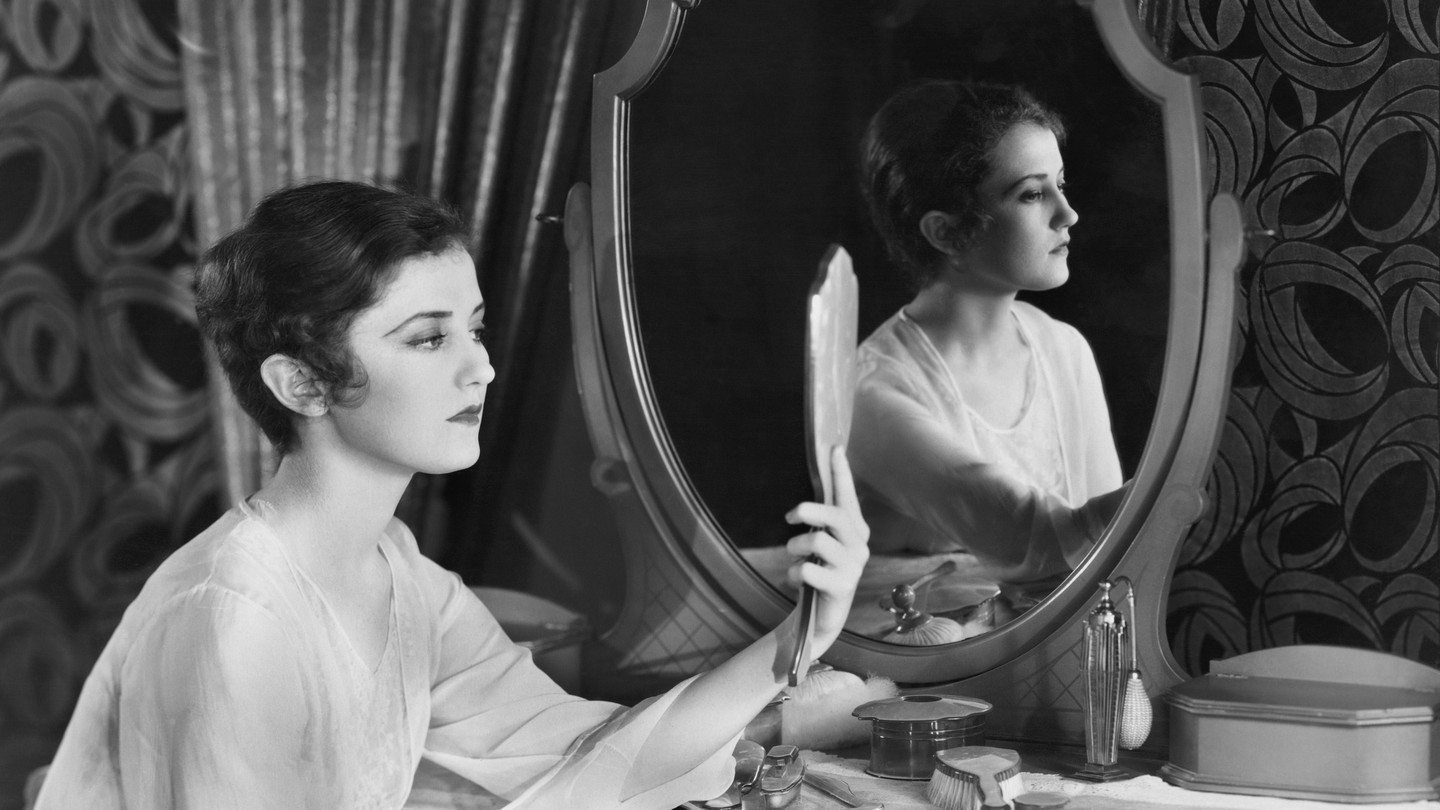 a black and white image of a woman staring in a mirror