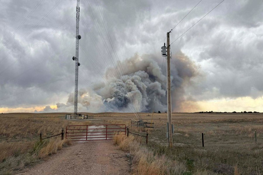 Smoke rises from a distant fire under a cloudy sky.