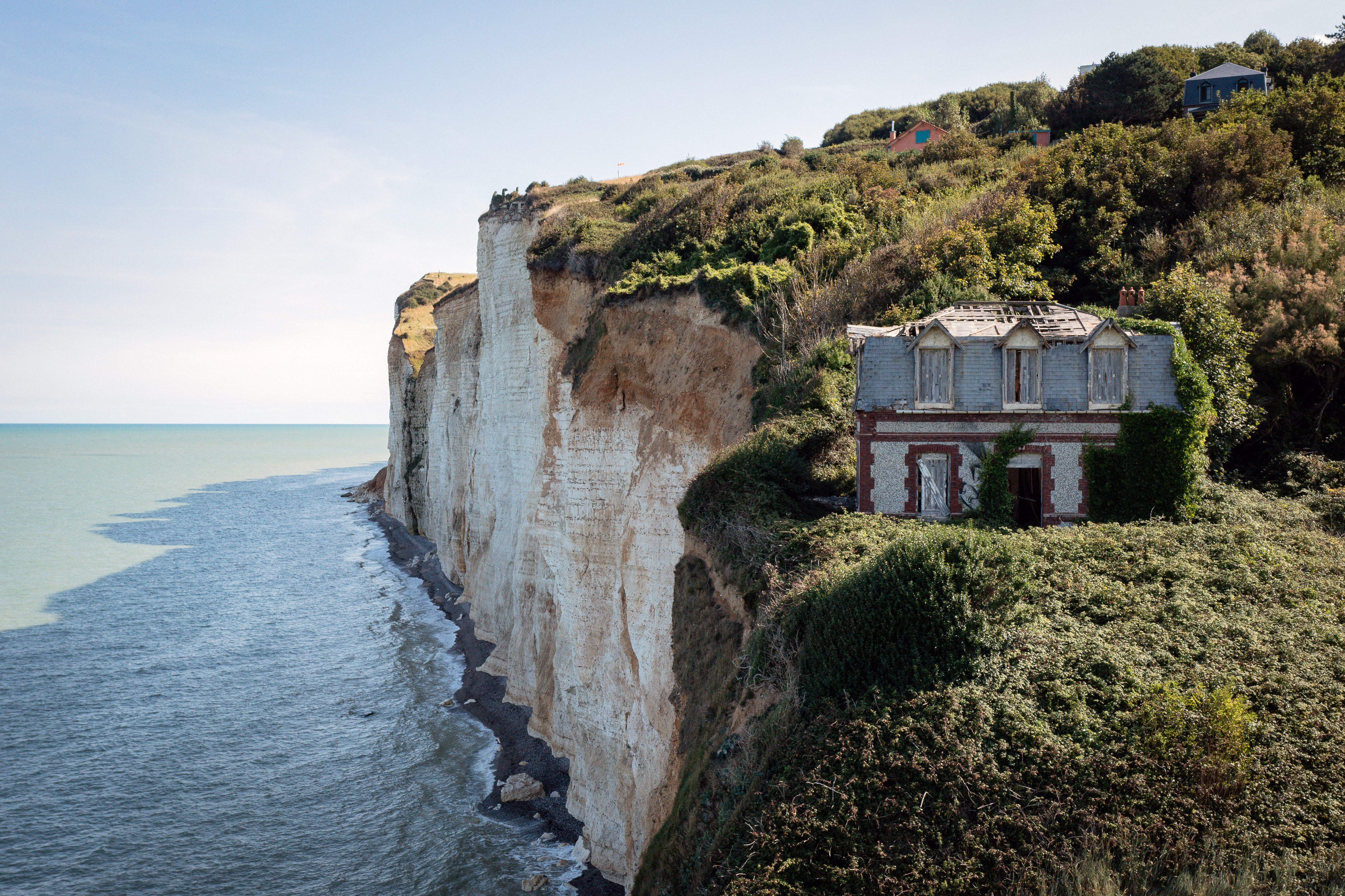 An abandoned house sits very close to steep, eroded cliffs.