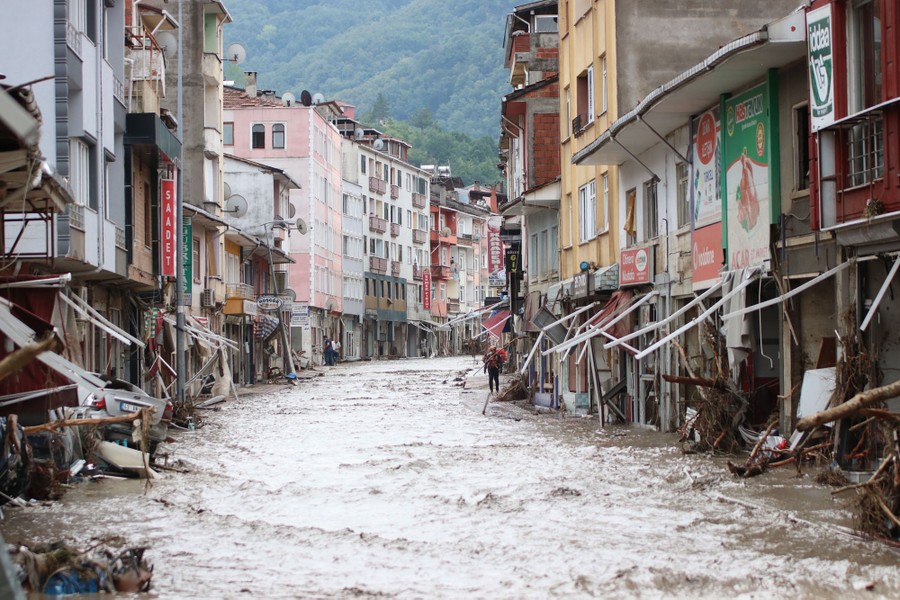 Floodwater flows down a road past damaged storefronts.