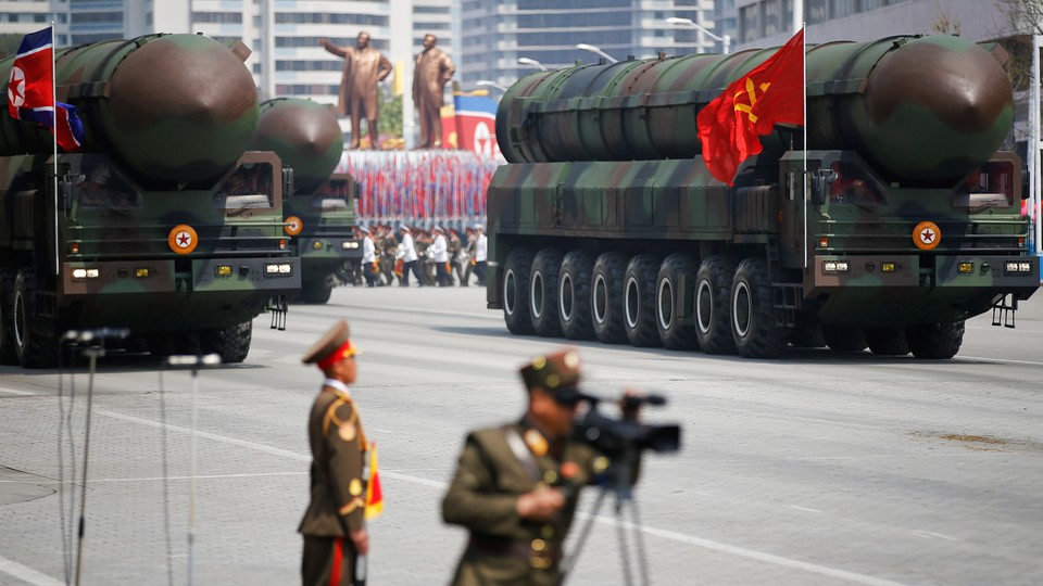 Intercontinental ballistic missiles are driven on military trucks with a North Korean military parade behind them