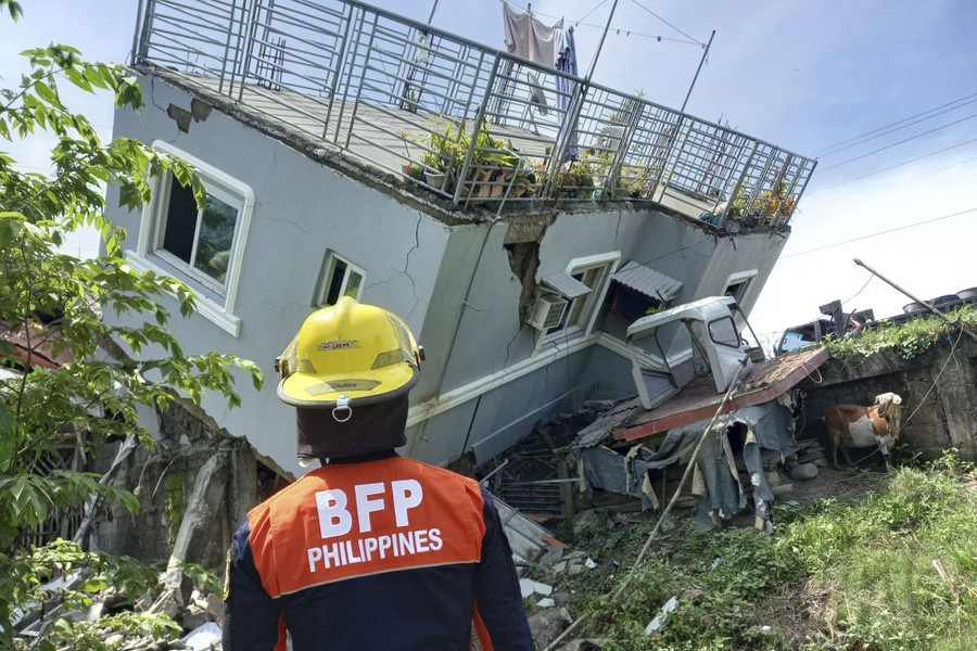 A rescue worker stands in front of a partially toppled house, after an earthquake.