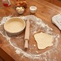 A cookbook next to a rolling pin and flattened dough 