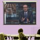 A projector screen is filled with a screengrab from John Oliver's show. The word "school" appears behind Oliver.