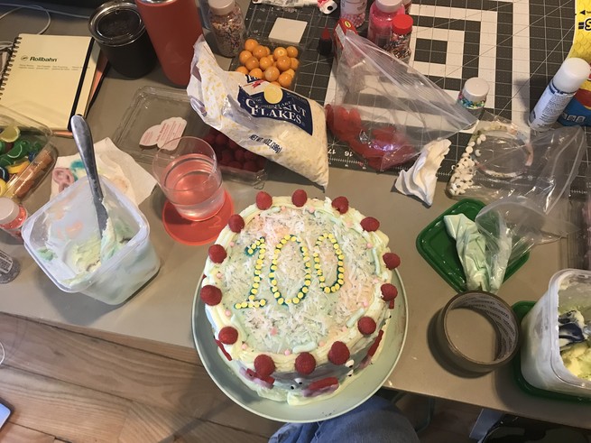A cake with "100" written on it, surrounded by cake-decorating supplies.