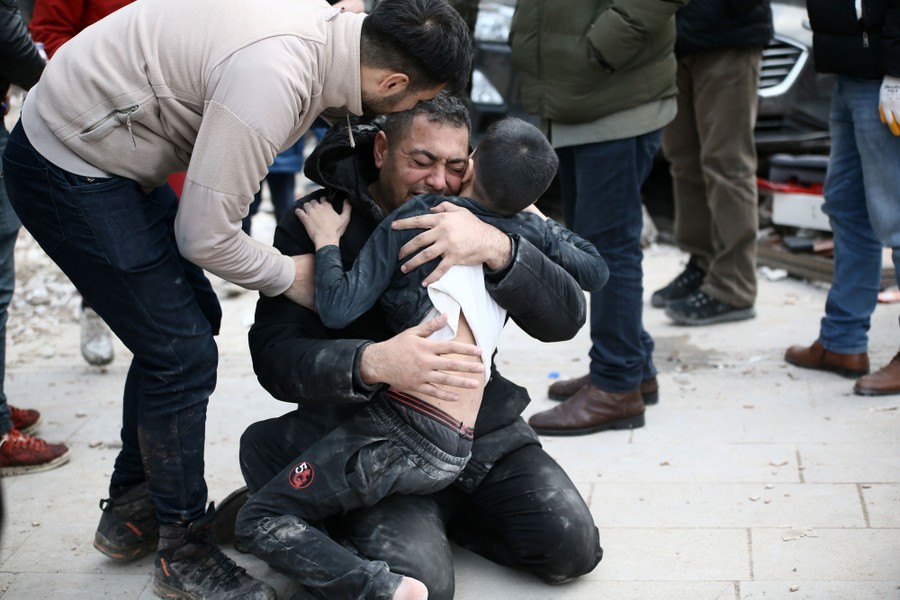 A man kneels on the ground, emotional, embracing a child who was just rescued from a collapsed building.