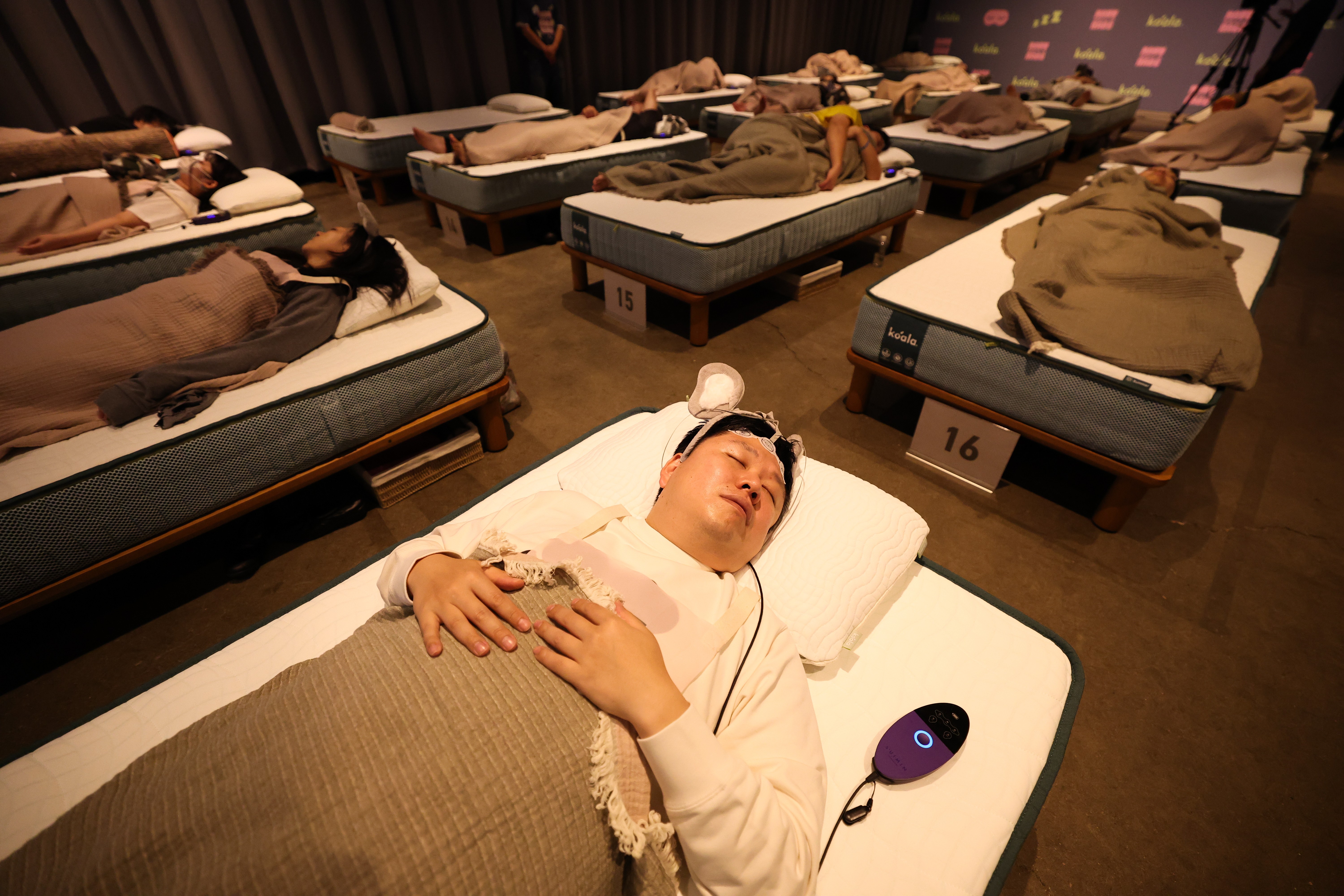 More than a dozen people lie in individual numbered beds during a sleep competition.
