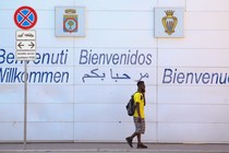 A person walks in front of a wall that says "Welcome" in different languages.