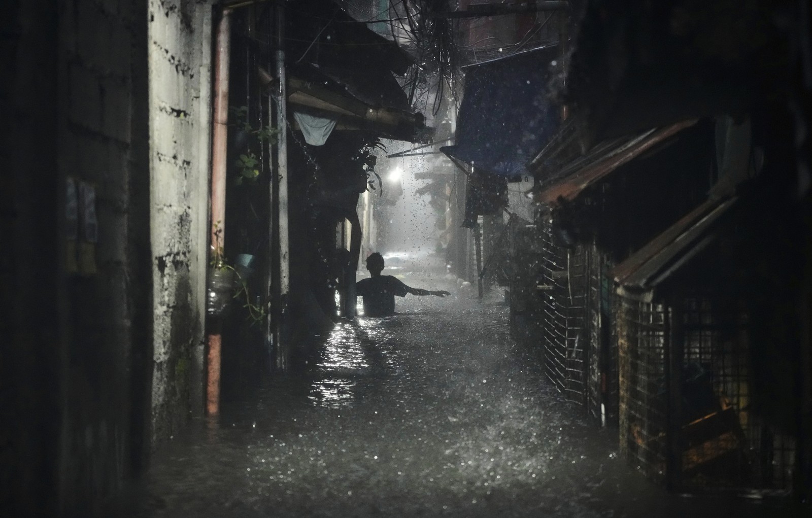 A person weighs through waist-deep floodwater in a narrow alleyway.