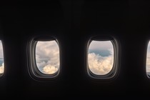 A row of airplane windows show a cloudy sky